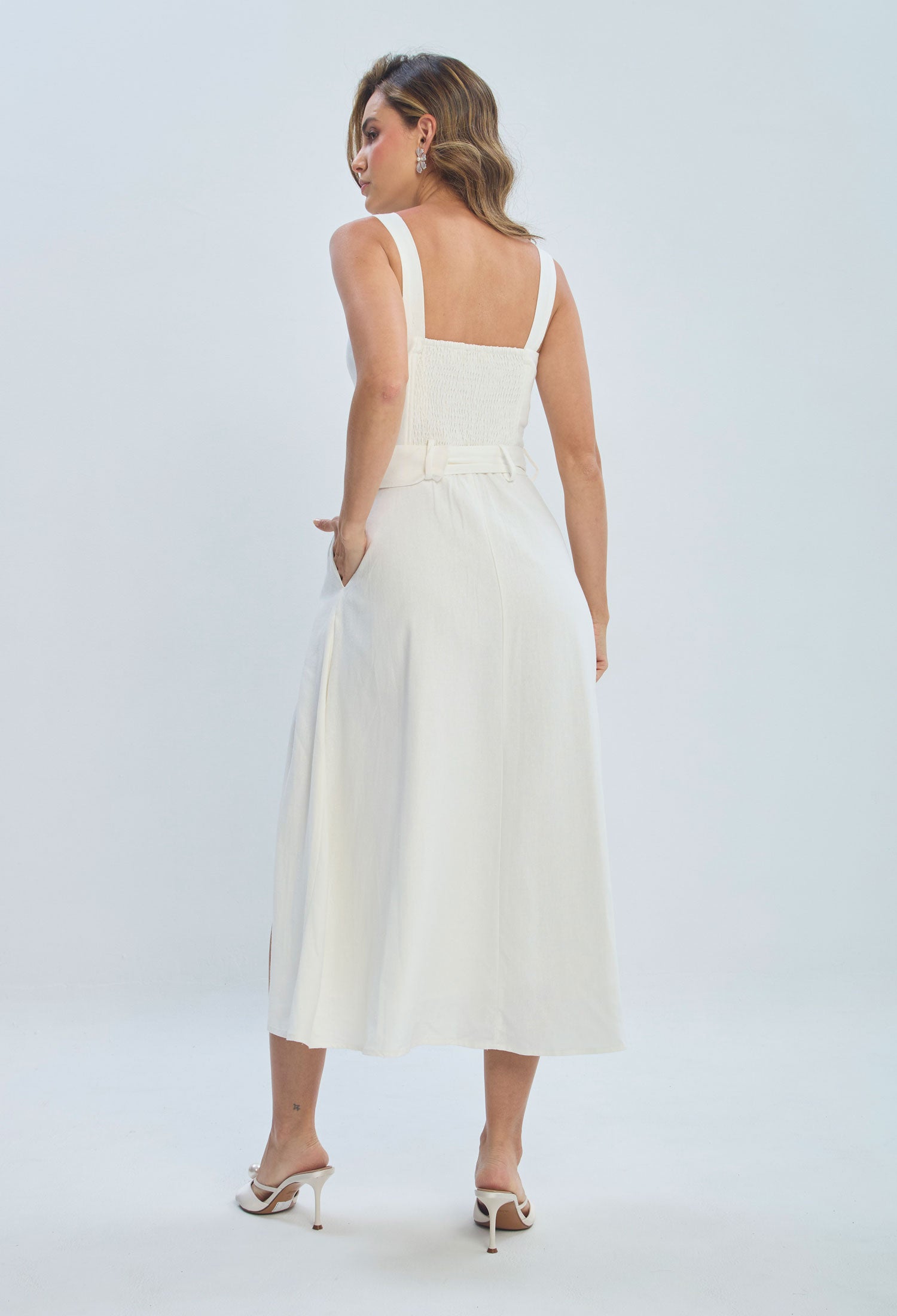 Woman wearing a sleeveless white midi dress with wide straps and belted waist, back view