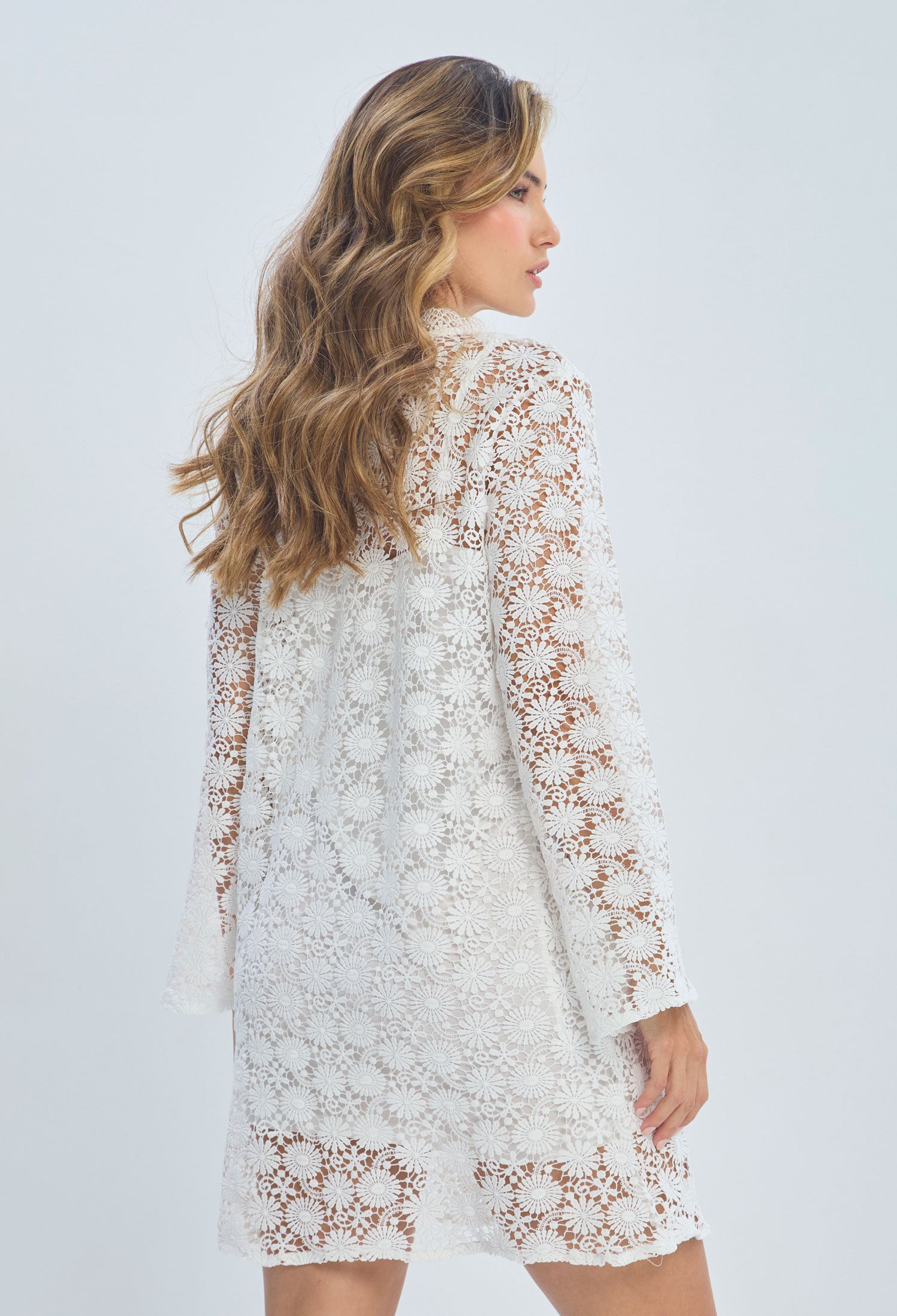 Woman wearing white long sleeve lace floral dress, side view, light background