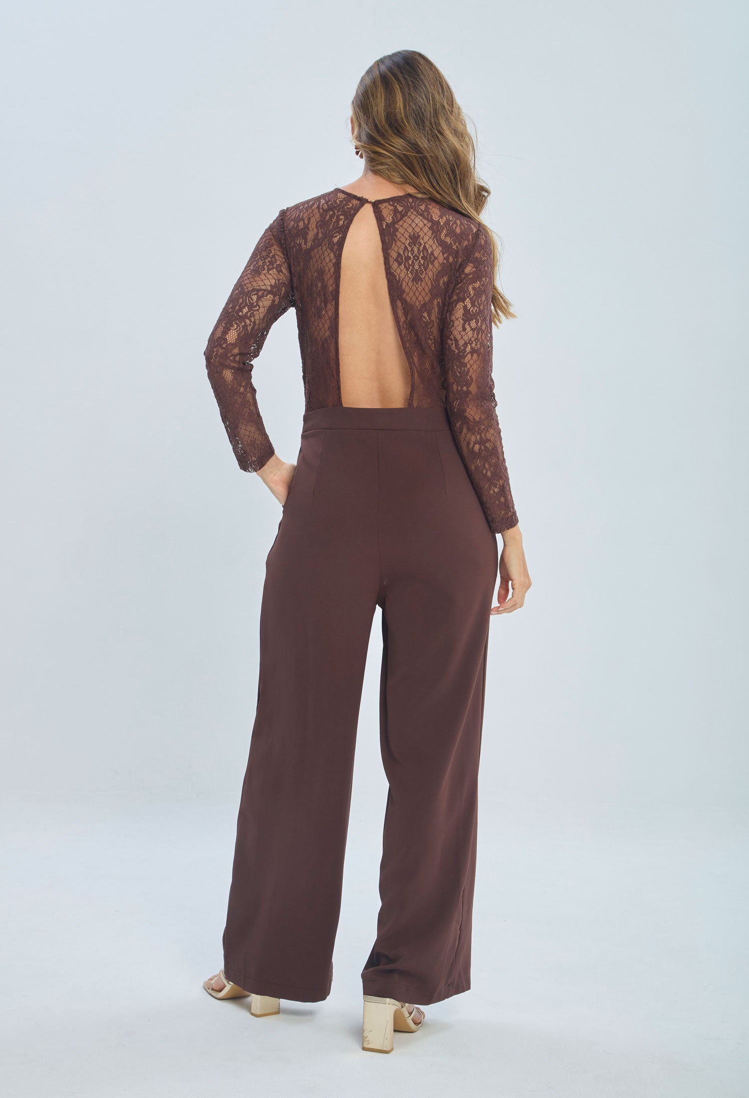Woman wearing brown lace long sleeve jumpsuit with open back and wide leg trousers