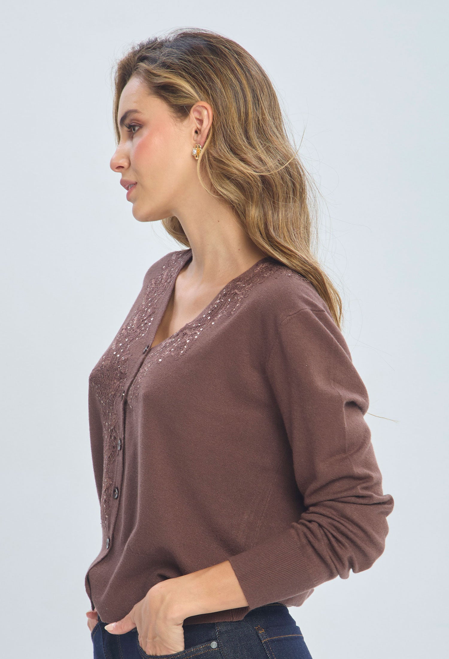 Woman wearing a brown V-neck buttoned sweater with sequin details and dark jeans