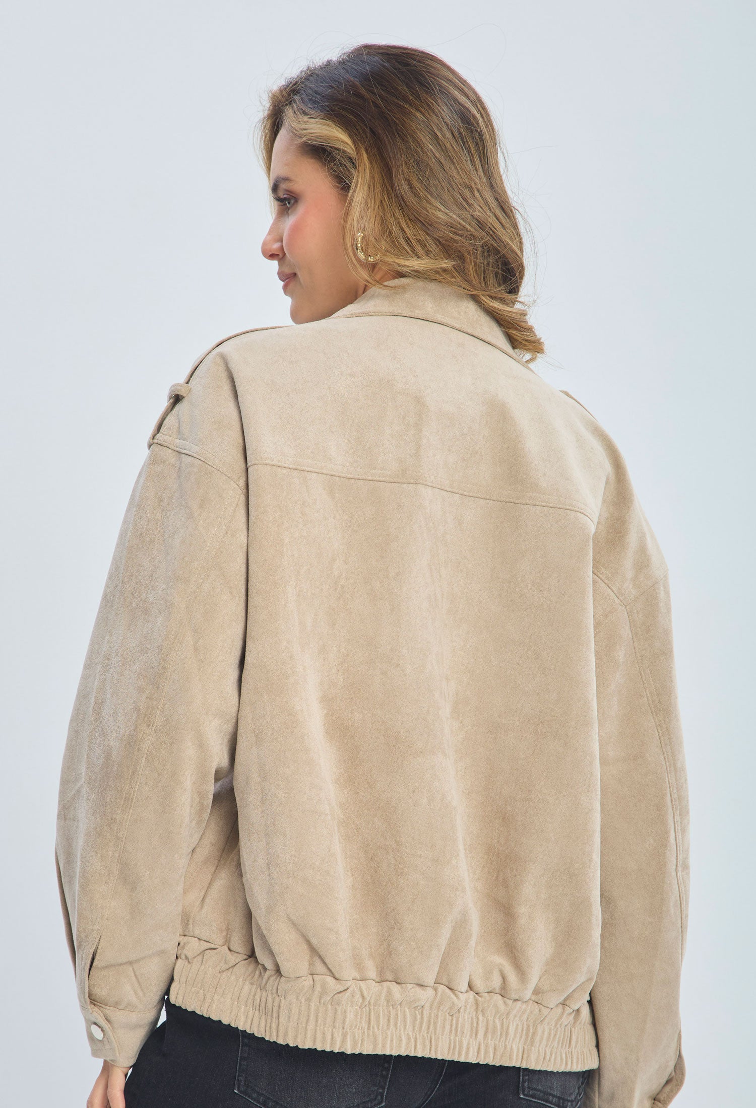 Woman wearing a beige suede jacket, shown from the back, with black jeans