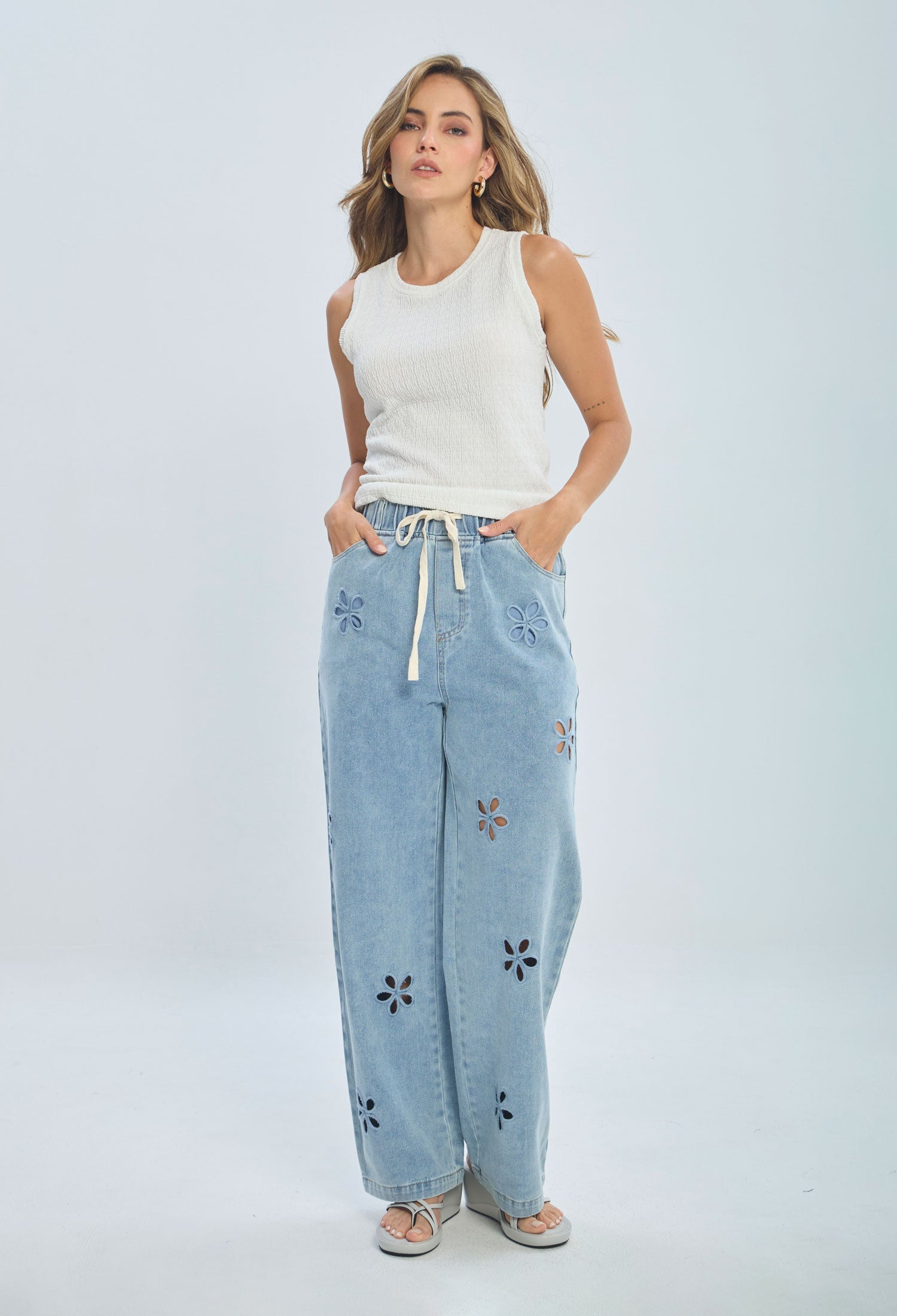 Woman wearing white sleeveless top and light blue wide-leg jeans with flower cutouts