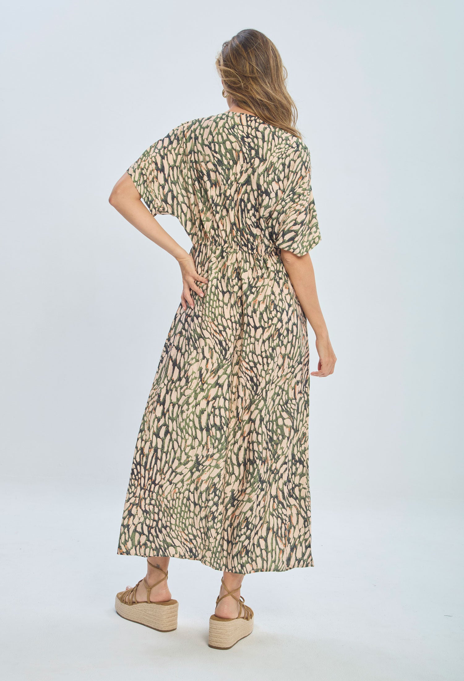 Woman in long patterned maxi dress with short sleeves and wedge sandals, back view