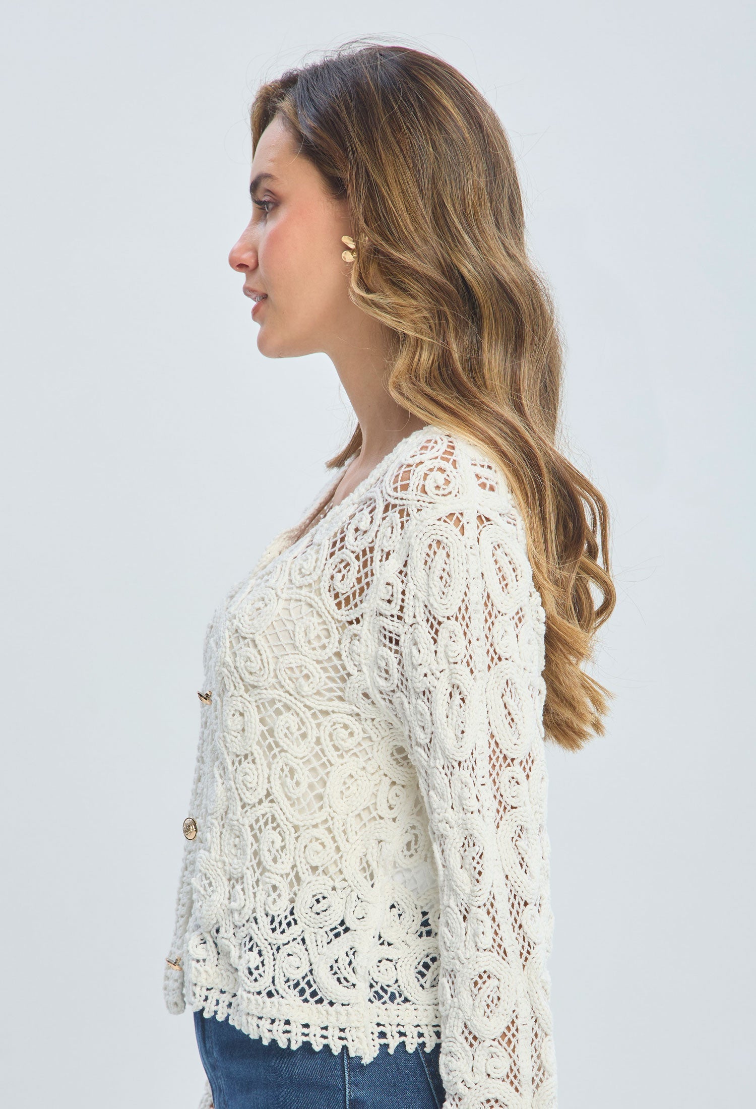 Woman in profile wearing a white lace long sleeve blouse and blue jeans