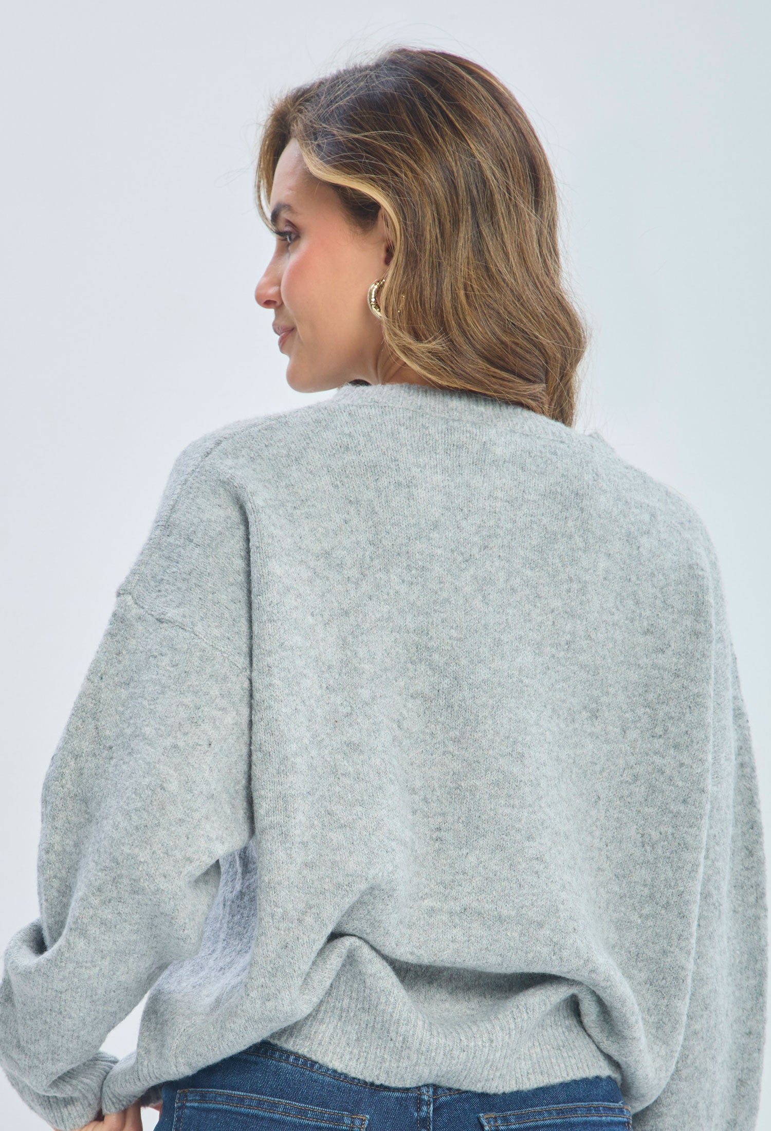Woman in a cozy light gray sweater and blue jeans, shown from the back