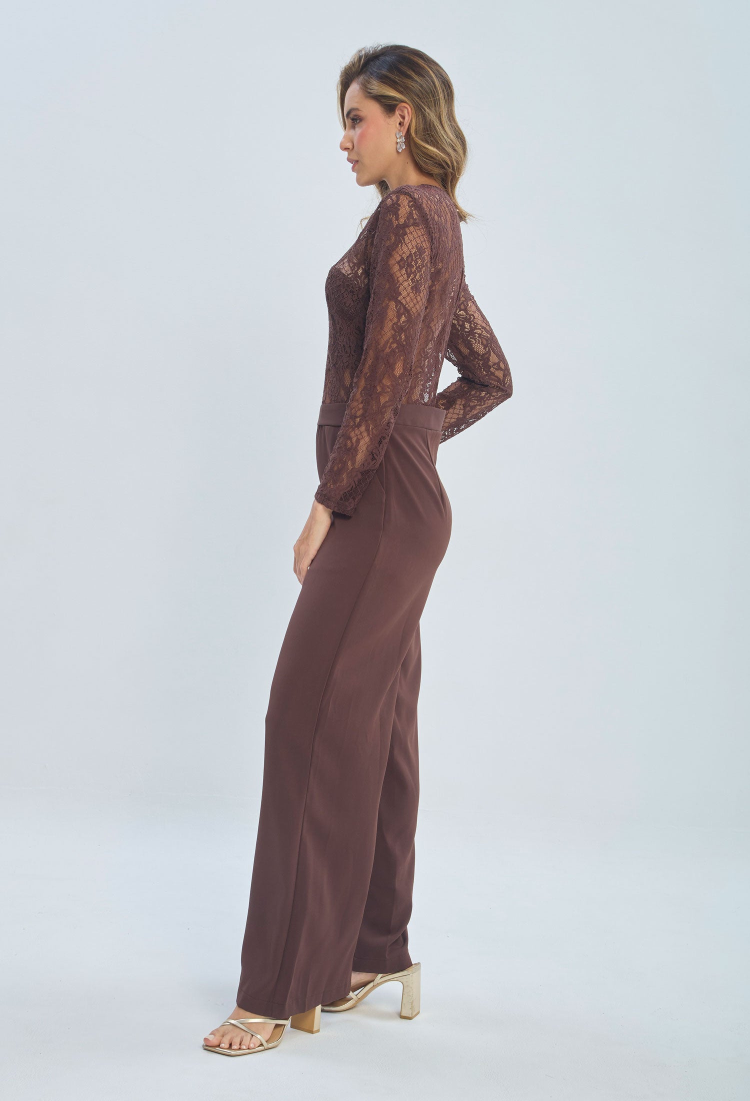 Woman in brown lace long sleeve jumpsuit with wide leg pants and gold heels
