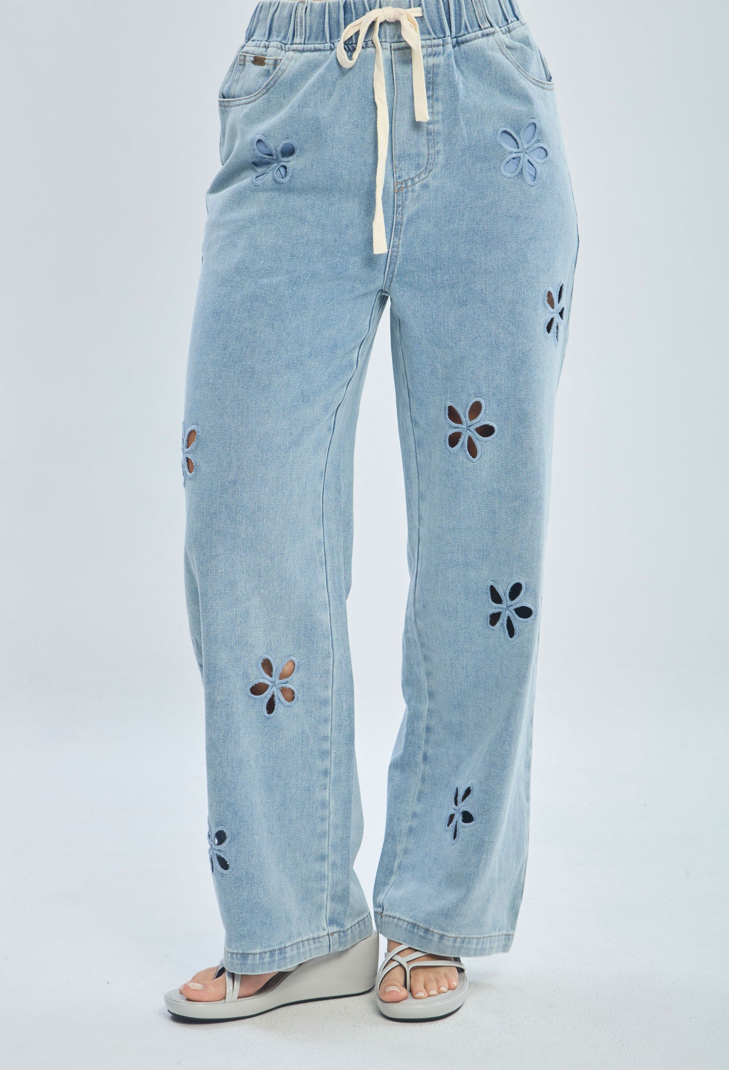 Light blue denim pants with floral cutouts, drawstring waist, and wide leg fit for women