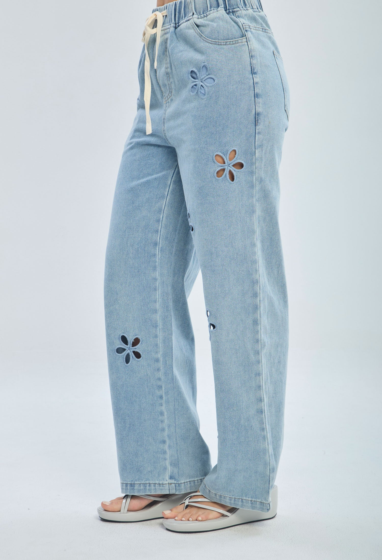 Light blue wide-leg jeans with floral cutout details and drawstring waist, modeled with sandals