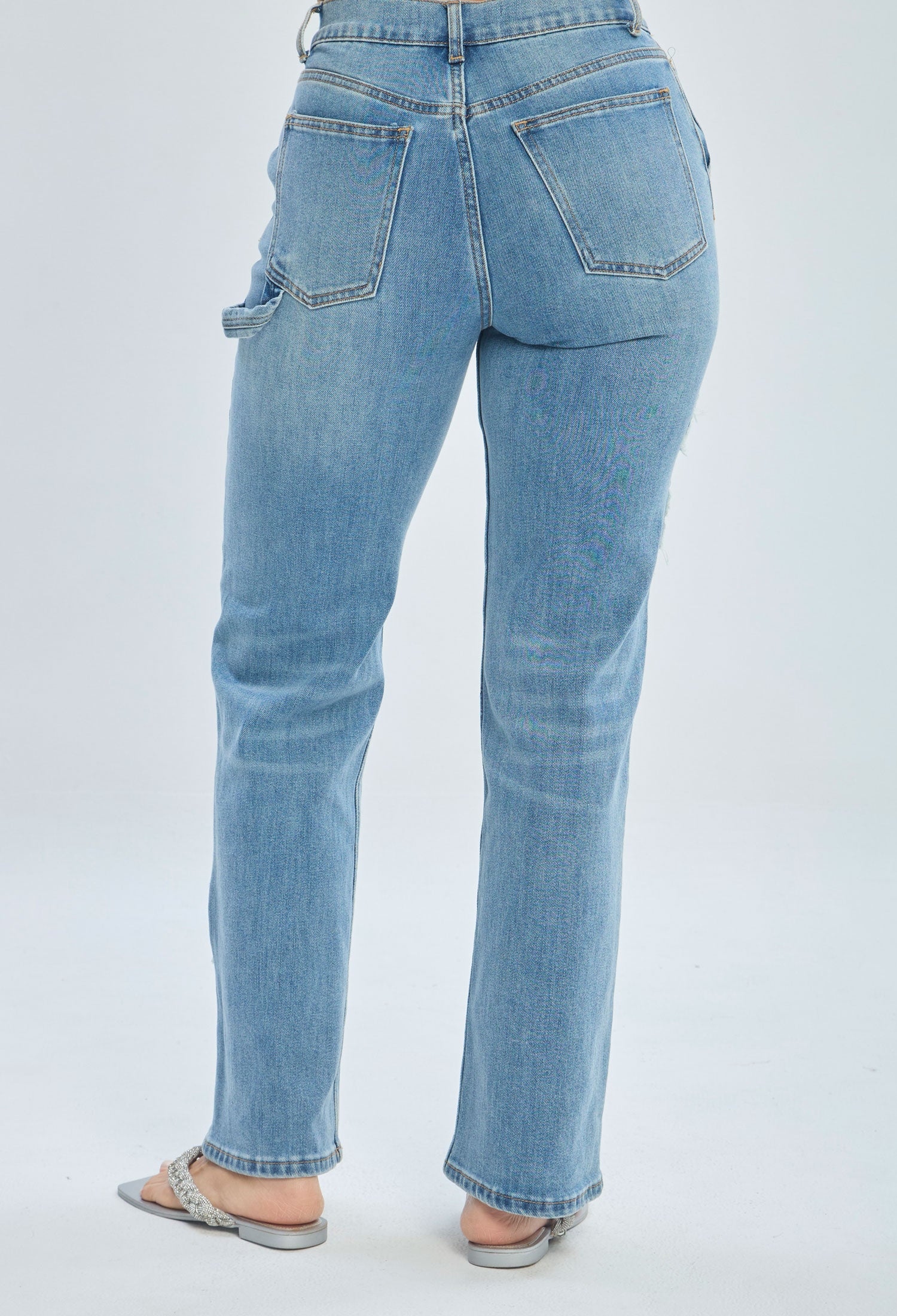 Back view of woman wearing light wash straight-leg jeans with pockets and silver sandals