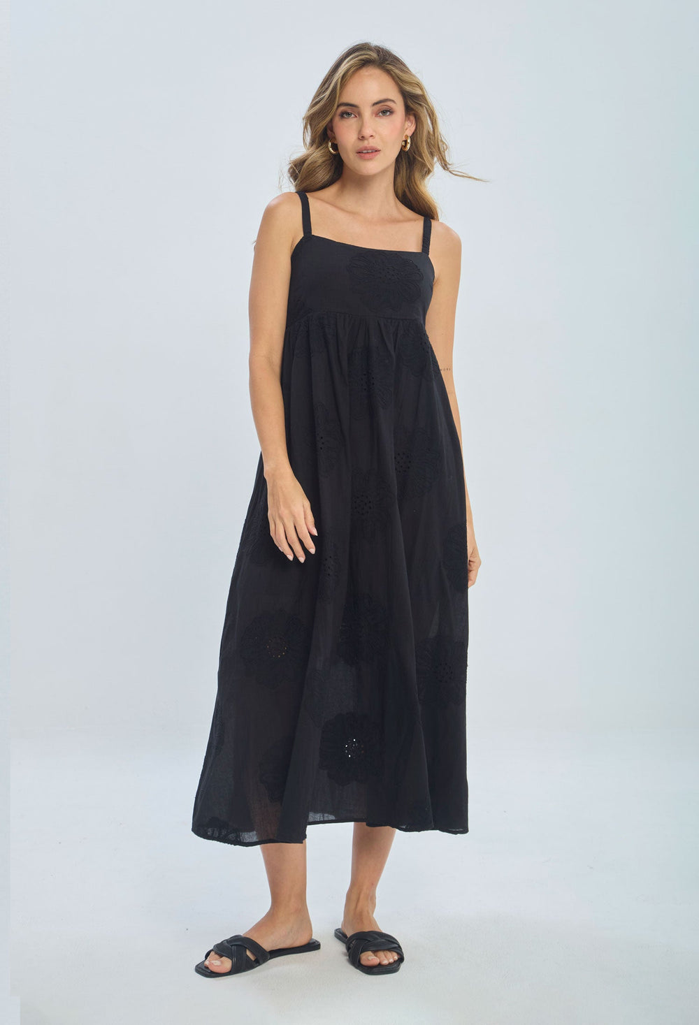 Woman wearing a sleeveless black midi dress with floral details and black sandals