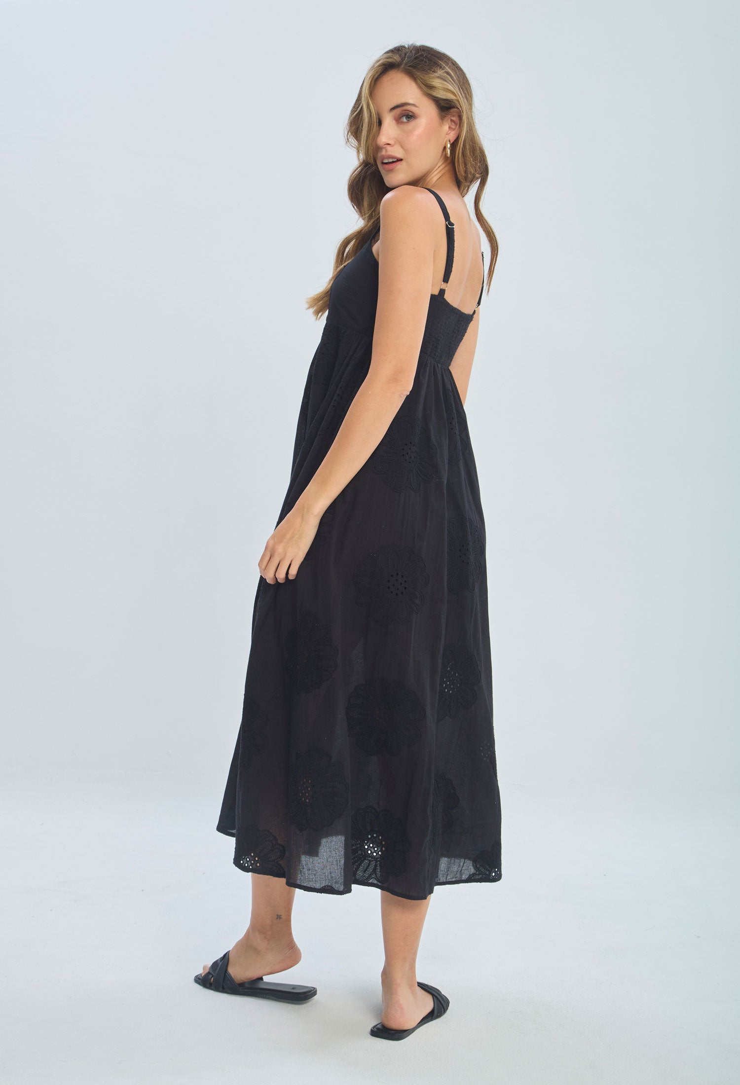 Woman in a black sleeveless midi dress with floral embroidery and open back, fashion studio shot