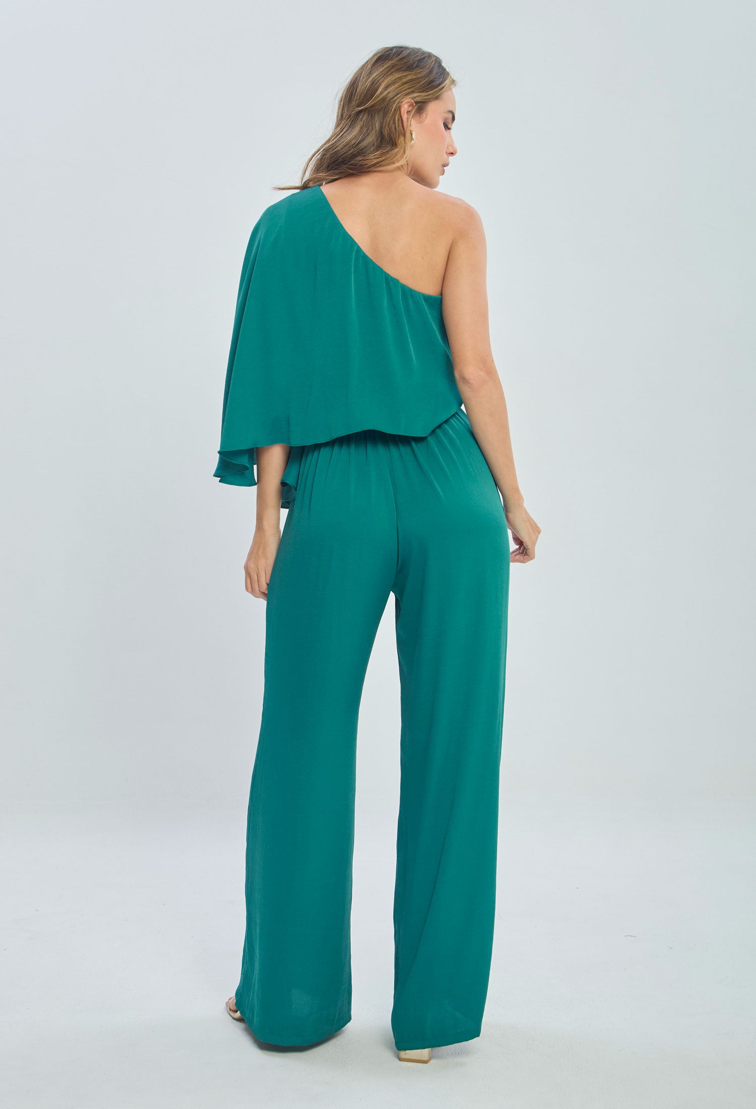 Woman wearing teal one-shoulder wide leg jumpsuit, back view, fashion photography