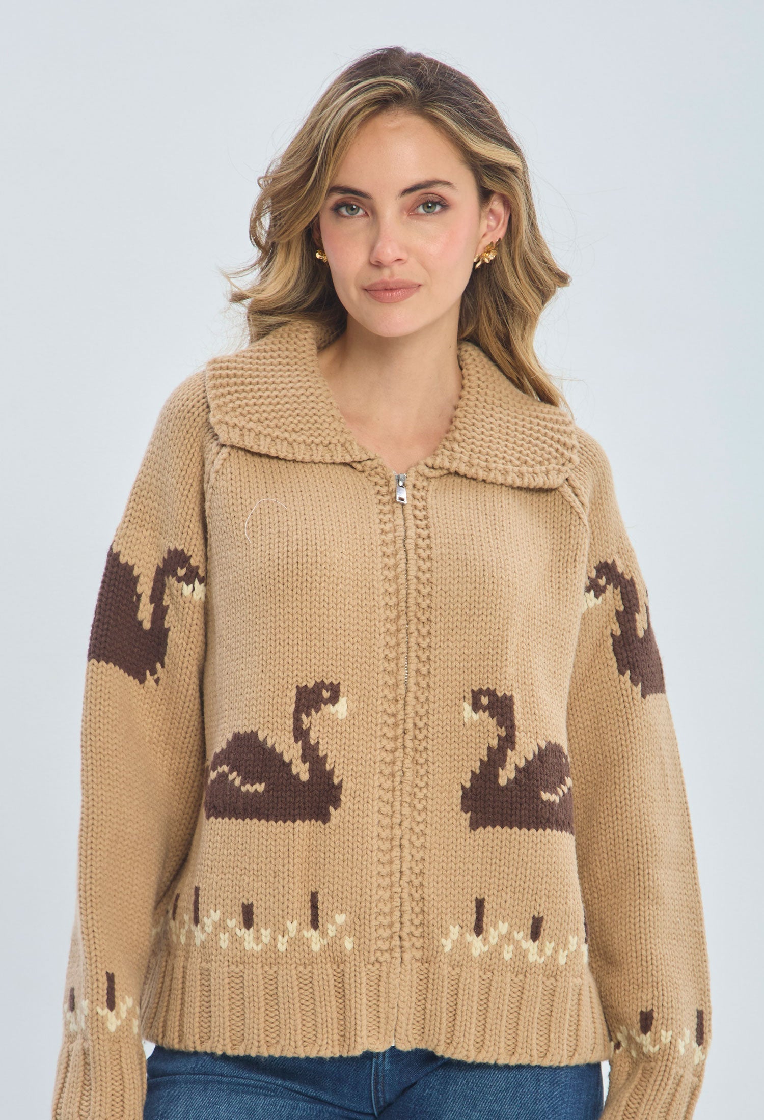 Woman wearing beige knitted zip-up sweater with brown swan pattern, blue jeans