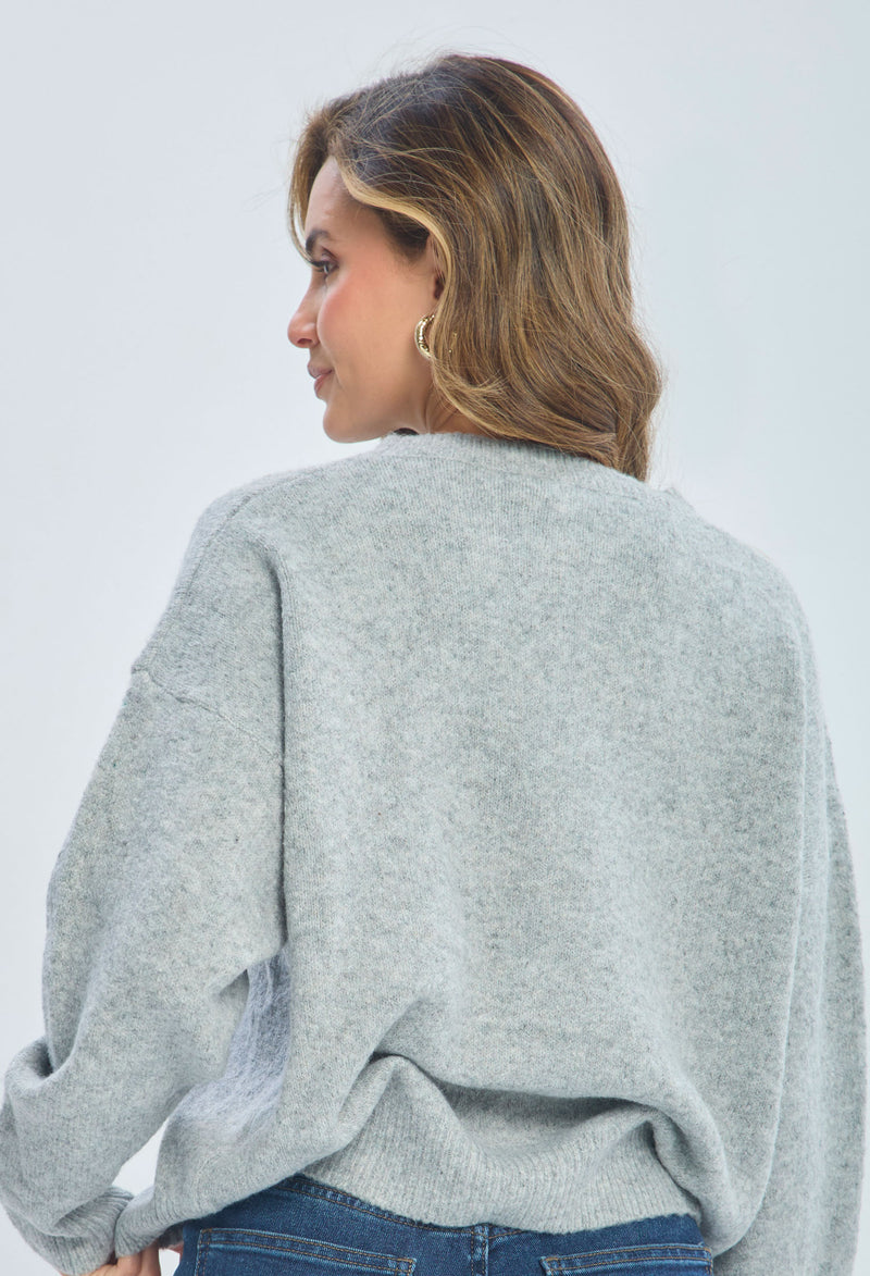 Woman in a cozy light gray sweater and blue jeans, shown from the back