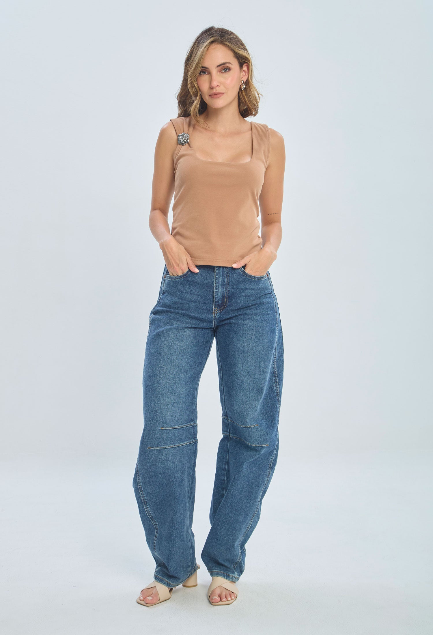 Woman in casual fashion wearing beige sleeveless top with brooch and blue wide-leg jeans
