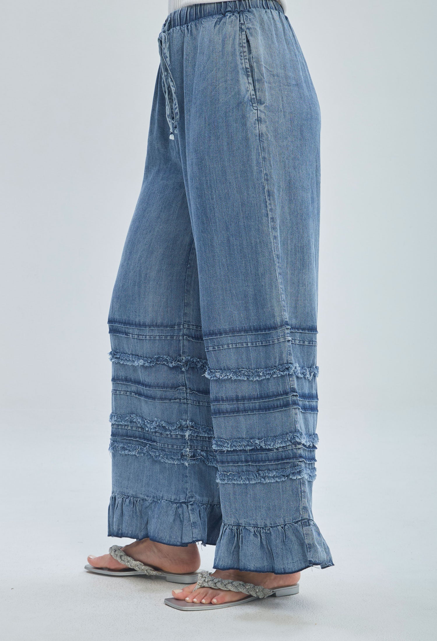 Wide leg denim pants with frayed horizontal details and ruffled hem, worn with sandals.